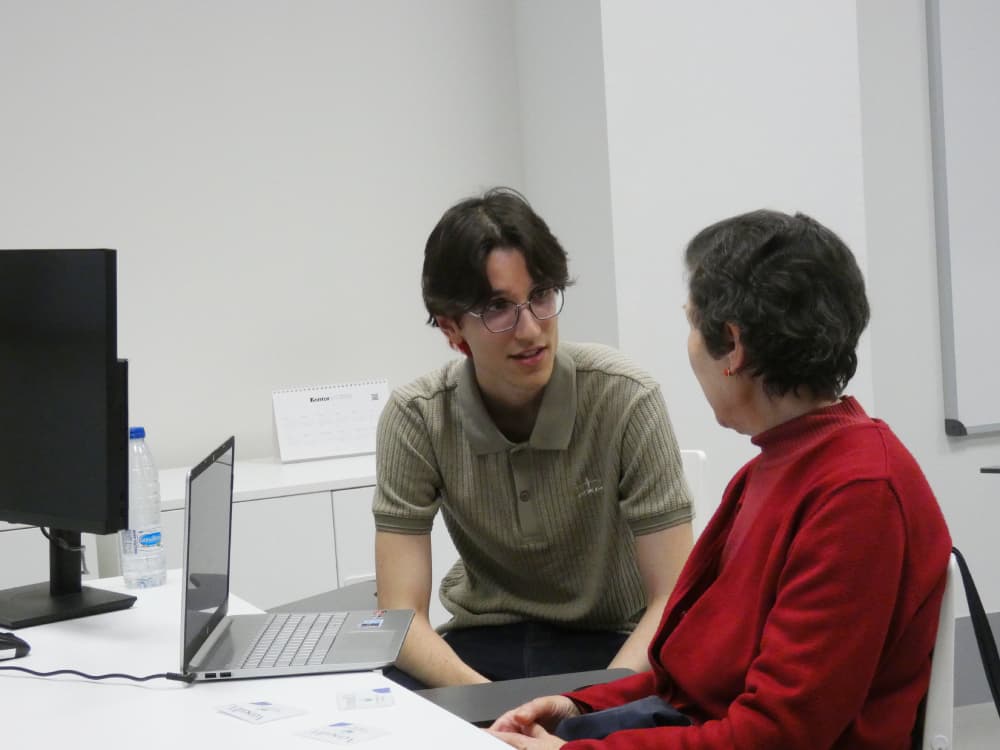 Membre de Versedia assis en conversation avec une personne âgée, lui montrant le résultat de sa biographie.