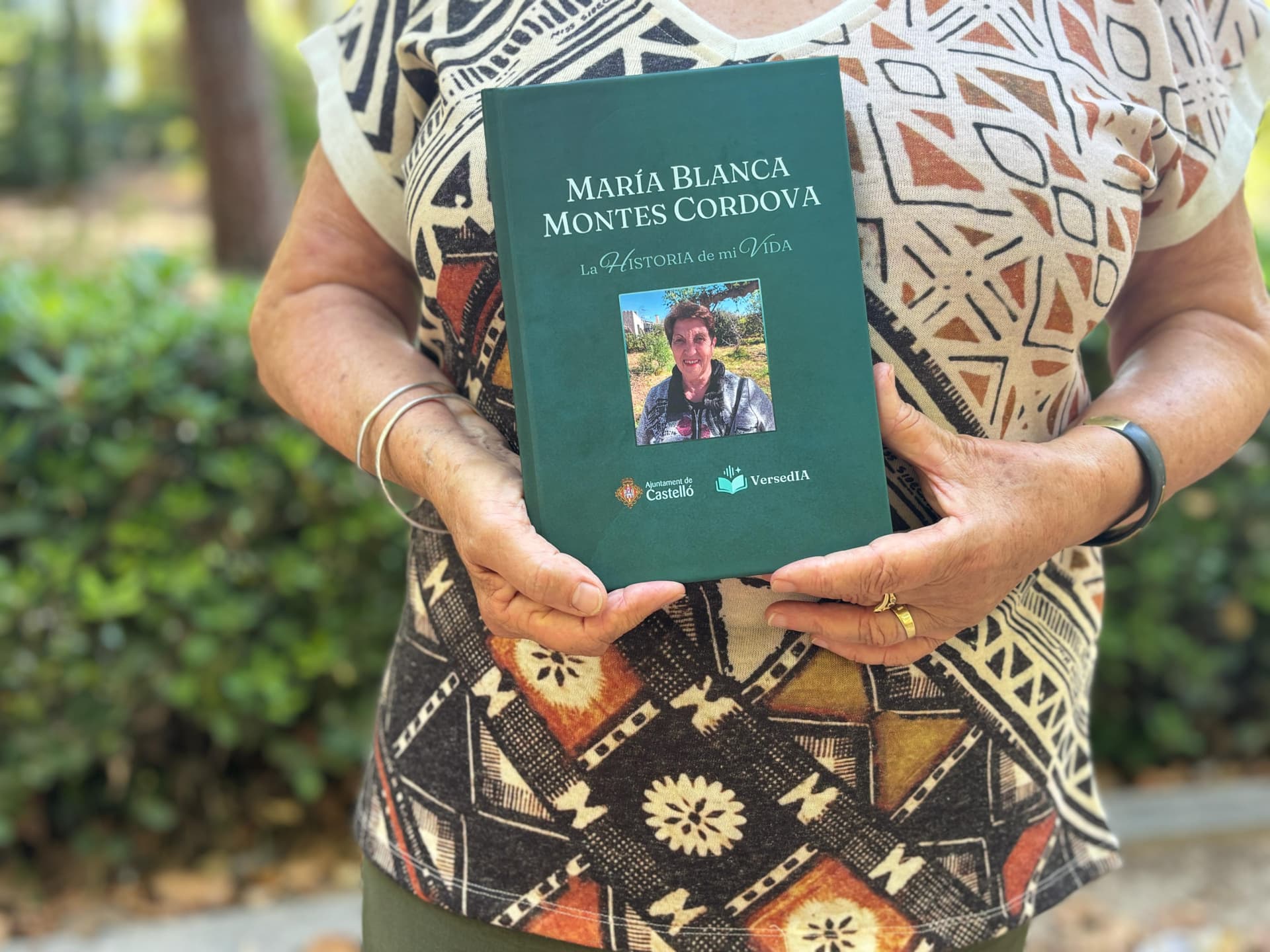Veïna de Castelló sostenint la seua biografia impresa, amb els segells de l'Ajuntament de Castelló i Versedia a la portada